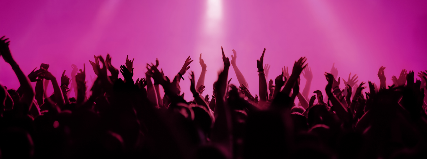klatschende Hände auf einem Konzert heben sich schwarz vor einem pinken Hintergrund ab